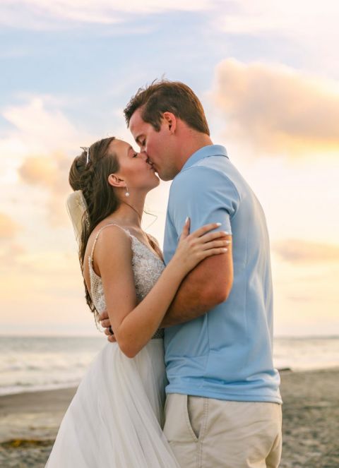 A newlywed couple kisses on the beach at sunset