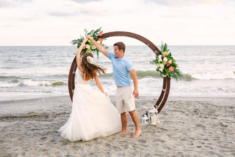 An elopement on Folly Beach, South Carolina - the couple twirls in front of their ceremony location with the ocean in the background of the photo.
